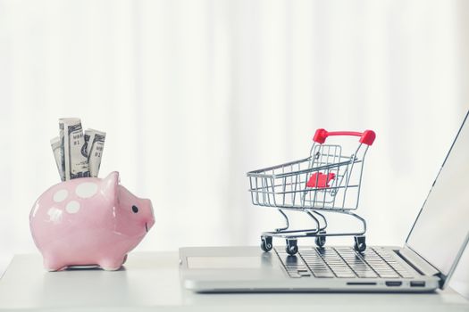 shopping cart and piggy bank with laptop on the desk, online shopping concept