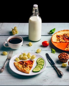 Healthy breakfast with frittata, fruits, vegetables, milk, cup of coffee and muffins on light wooden background.