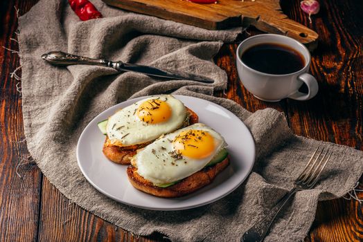 Bruschettas with vegetables and fried eggs on white plate and cup of coffee over grey rough cloth. Healthy food concept.