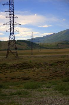 A power line with metal pillars runs through the valley to the mountains. Altai, Siberia, Russia