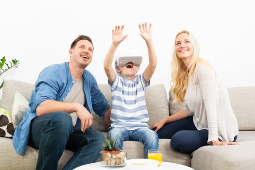 Happy caucasian family at home on living room sofa having fun playing games using virtual reality headset.