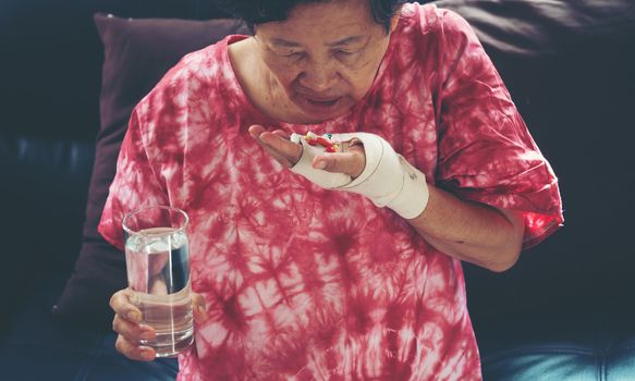 Senior asian woman take pill medicine on hand while sitting on sofa at home 