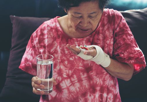 Senior asian woman take pill medicine on hand while sitting on sofa at home 