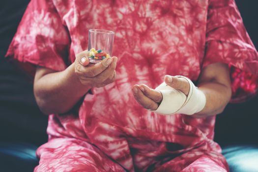 Senior asian woman take pill medicine on hand while sitting on sofa at home 