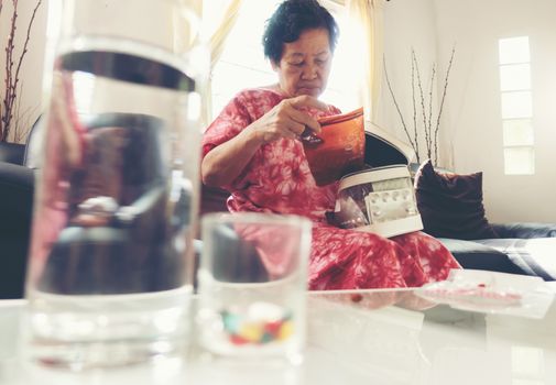 Senior asian woman take pill medicine on hand while sitting on sofa at home 