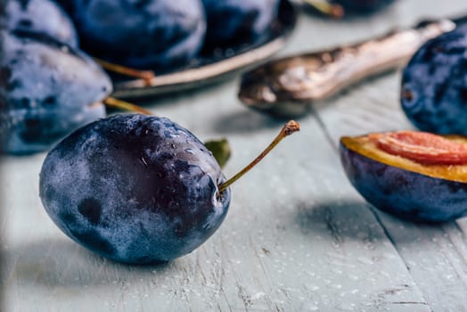 Ripe plums with sliced fruits, leaves and vintage knife over light wooden surface