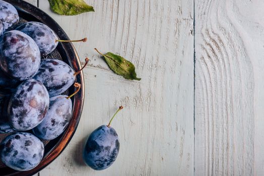 Ripe plums on metal plate over light wooden surface. Copy space