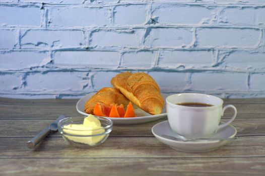 A traditional breakfast, a cup of black coffee, two croissants with butter and orange slices.