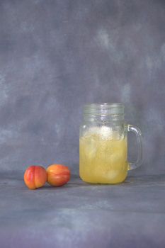 Two ripe tasty apricots lie near a mug with ice and juice.