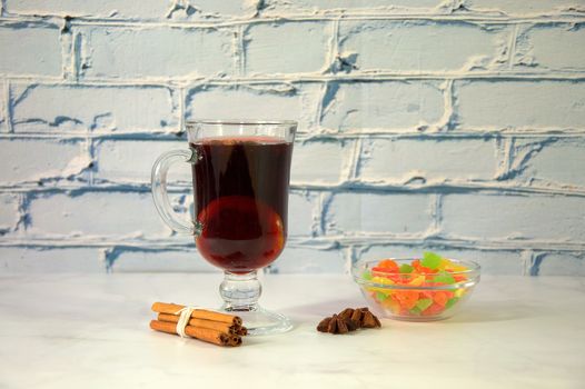 Glass cup with mulled wine and lemon with a bunch of cinnamon sticks, anise stars and a bowl of dried fruit.