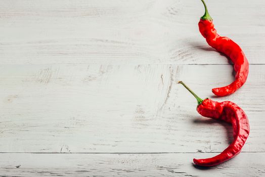 Two red chili peppers over light wooden background.