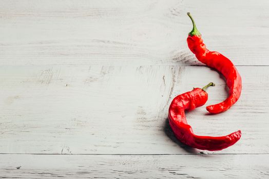 Two ripe chili peppers over white wooden background.