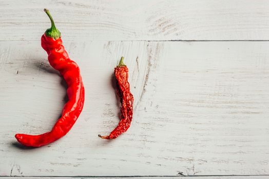 Two red chili peppers, fresh and dry, over wooden background