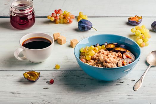 Healthy breakfast concept. Porridge with fresh plum, green grapes and cup of coffee.