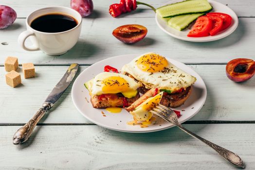 Breakfast toasts with vegetables and fried egg on white plate, cup of coffee and some fruits over wooden background. Clean eating food concept.