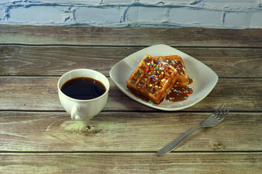 A cup of black coffee and a plate with two Viennese waffles on a wooden table.