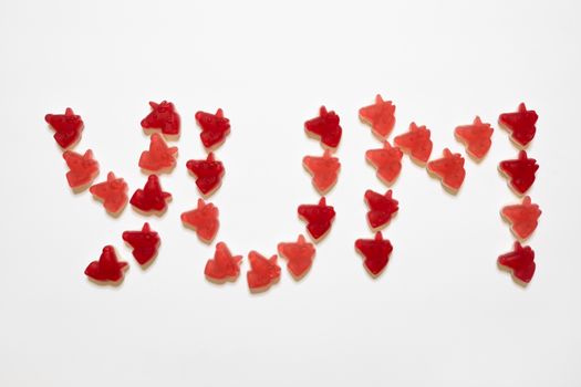 Yum inscription consisting of marmalade unicorns laid out on white background. Concept of healthy natural sweets, joy, childhood, sugar free or unhealthy nutrition. Flat lay, close-up.