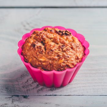 Cooked oatmeal muffin in a pink silicone bakeware over light wooden background.