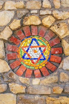 Circular mosaic religious symbol Star of David on stone wall.