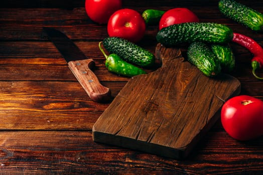 Fresh cucumbers, tomatoes and chili peppers on cutting board for preparing salad.