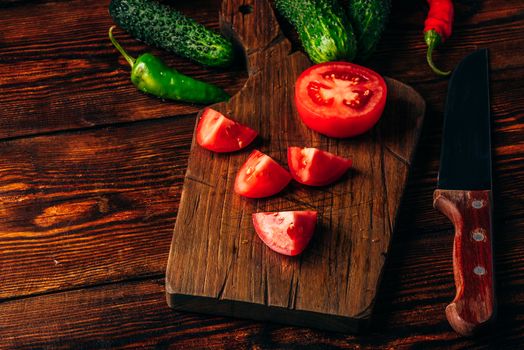 Sliced tomatoes on cutting board and cucumbers with chili peppers over wooden background.