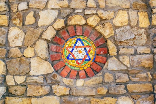 Circular mosaic religious symbol Star of David on stone wall.