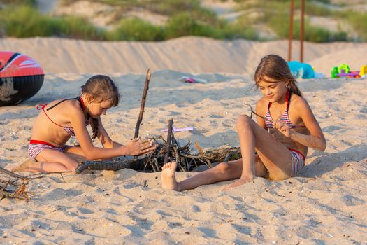 Two girls in the evening on the beach prepare a place for a fire