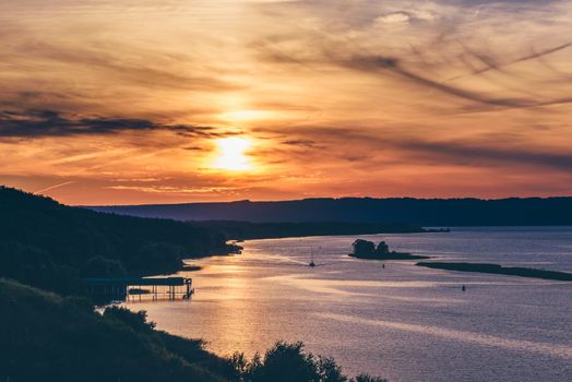 Summer sunset on river shore. Sailing boat on river.