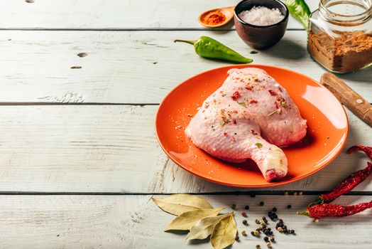 Chicken leg quarter on orange plate over wooden surface with different spices