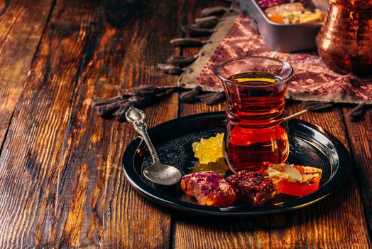 Tea in armudu glass with oriental delight rahat lokum on metal tray over wooden surface and tablecloth