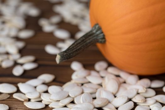 Fresh orange pumpkin and pimpkin seeds close-up on wooden background