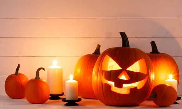 Halloween pumpkin head jack o lantern and candles on wooden background