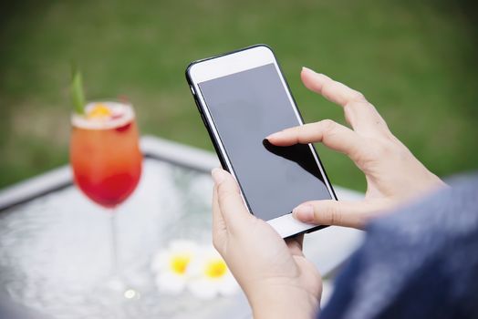 Lady using mobile phone relax in green garden with soft drink background - people and technology lifestyle concept