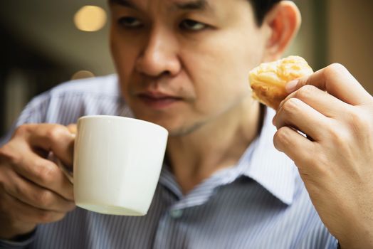 Sleepy man drinking coffee with bread - people with caffeine coffee drink concept