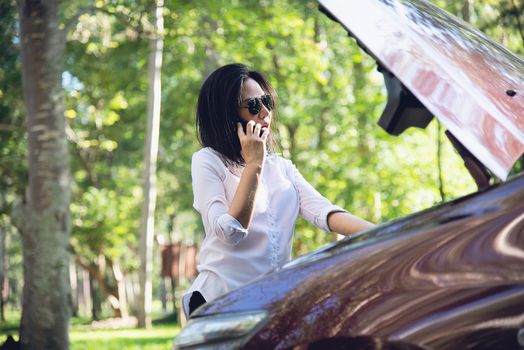 Asian woman calling repairman or insurance staff to fix a car engine problem on a local road - people with car problem transportation concept 