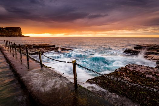 Coastal sunrise by the ocean rock pool  with tidal flows over rocks and flowing into the pool