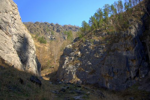 A trail in a mountain gorge, among the hillsides covered with forest and grass.