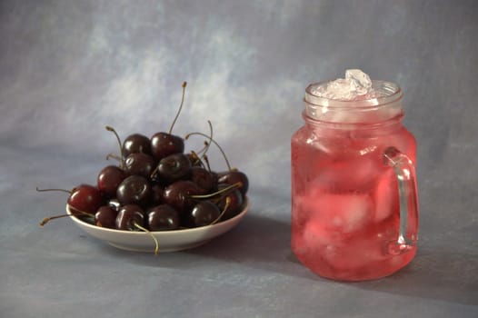 A full saucer of ripe fresh cherries and a glass mug with cherry juice with ice.