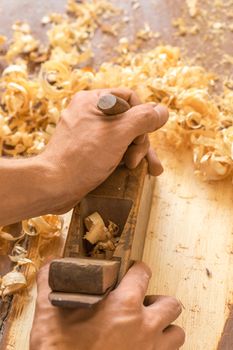Closeup of woodworker's hands shaving with a plane in a joinery workshop