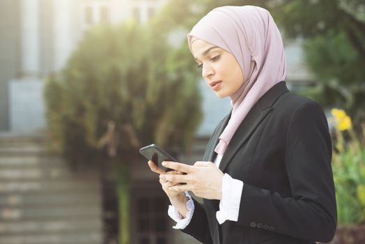 Muslim business woman walking and using smart phone.