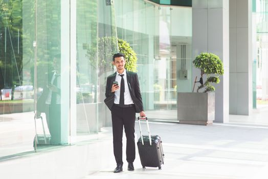 Busy Asian businessman with luggage walking to airport, checking schedule from smartphone.