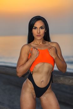 Fitness girl posing 
in the shore of the beach with a beautiful black and orange bikini