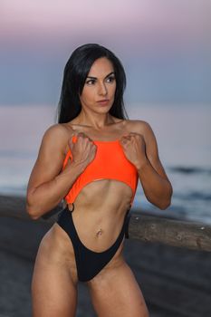 Fitness girl posing 
in the shore of the beach with a beautiful black and orange bikini