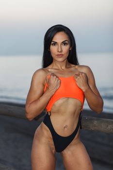 Fitness girl posing 
in the shore of the beach with a beautiful black and orange bikini