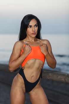 Fitness girl posing 
in the shore of the beach with a beautiful black and orange bikini