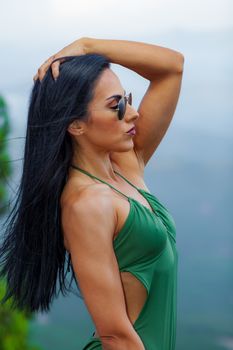 Fitness girl posing in the beach forest with a beautiful green swimsuit and sunglasses