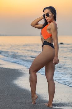 Fitness girl posing 
in the shore of the beach with a beautiful black and orange bikini and sunglasses