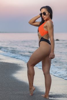 Fitness girl posing 
in the shore of the beach with a beautiful black and orange bikini and sunglasses