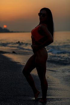 Fitness girl posing 
in the shore of the beach with a beautiful black and orange bikini and sunglasses