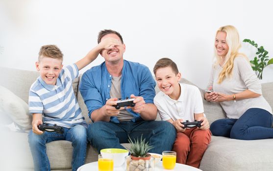 Happy young family playing videogame console on TV. Spending quality leisure time with children and family concept. Gaming consoles are generic and debranded.